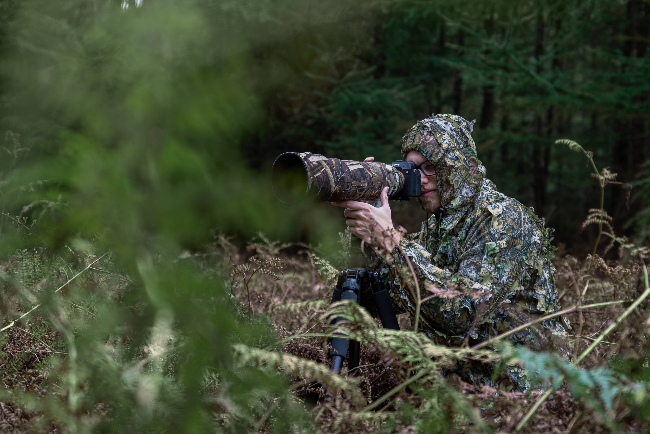 Rainer Lentjes wildlife and nature photographer wearing camouflage clothing hiding in dense forest.