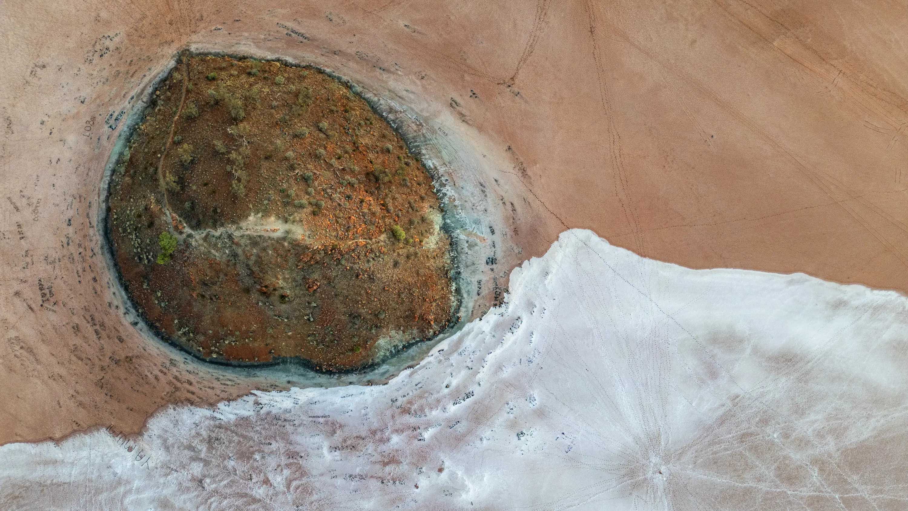 Aerial view of a small island surrounded by red and white salt flats in outback Australia.