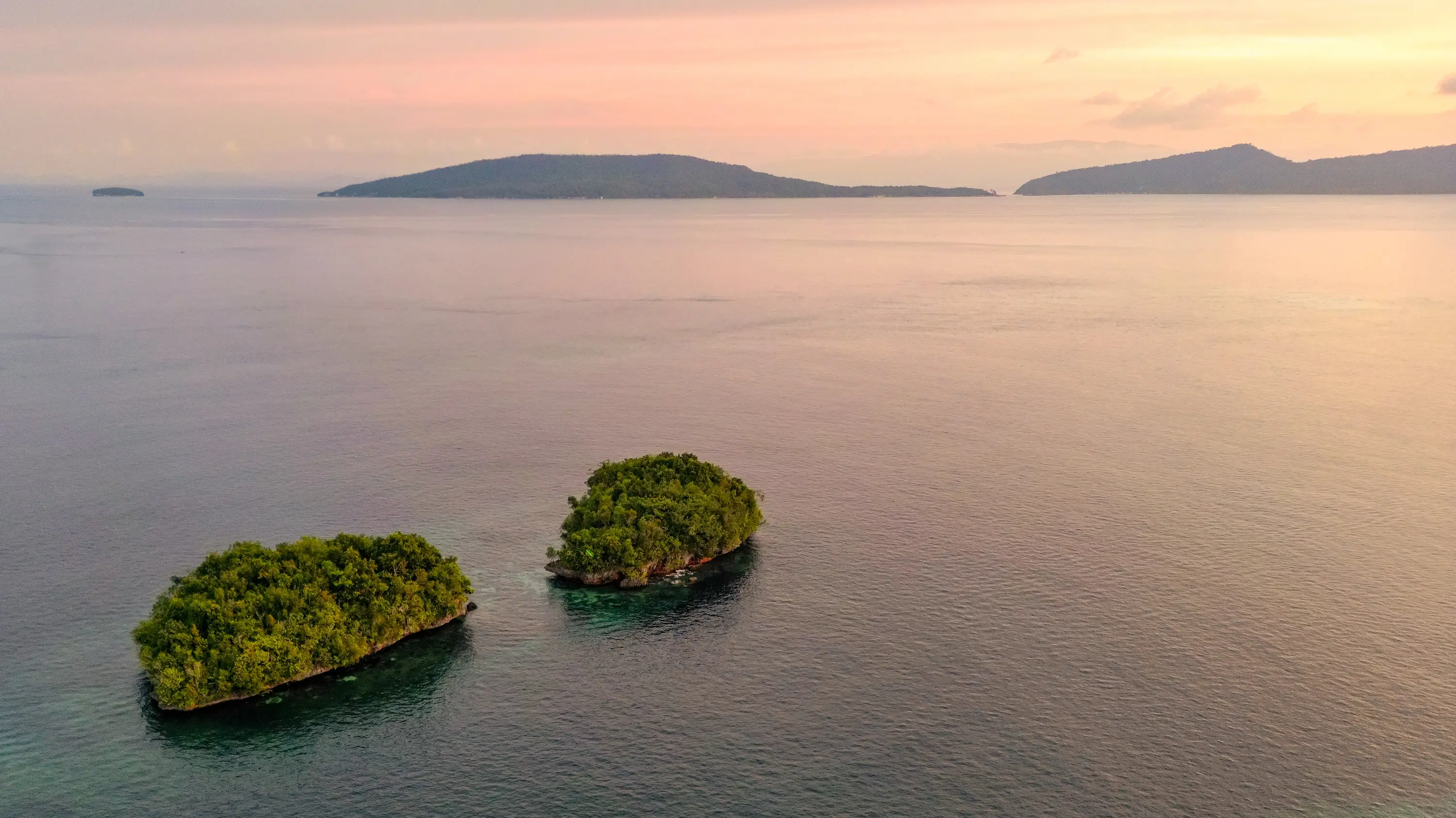 Tropical islands surrounded by calm ocean at sunset in Raja Ampat, Indonesia.