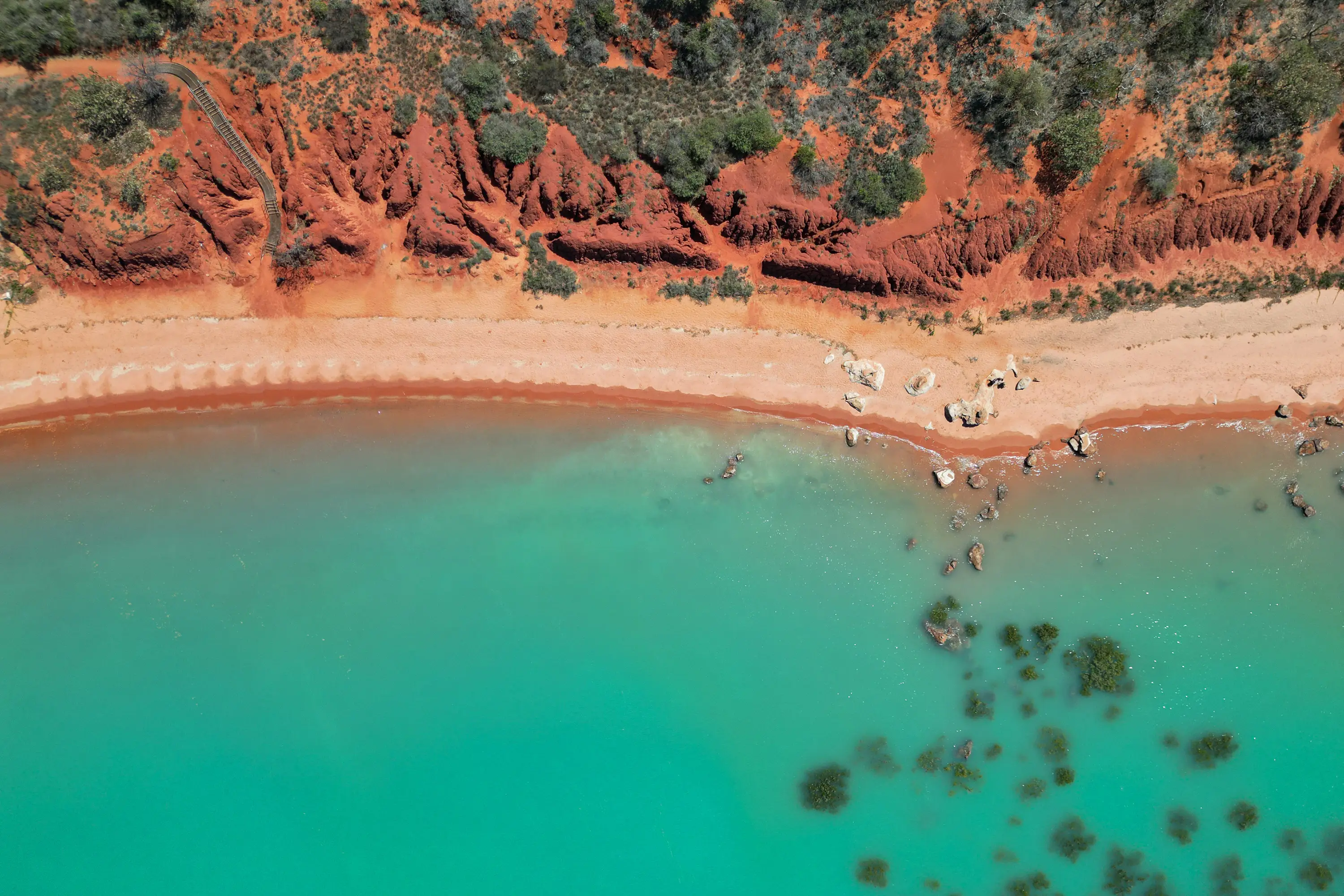 Aerial view of turquoise water meeting red coastal cliffs near Broome, Western Australia.